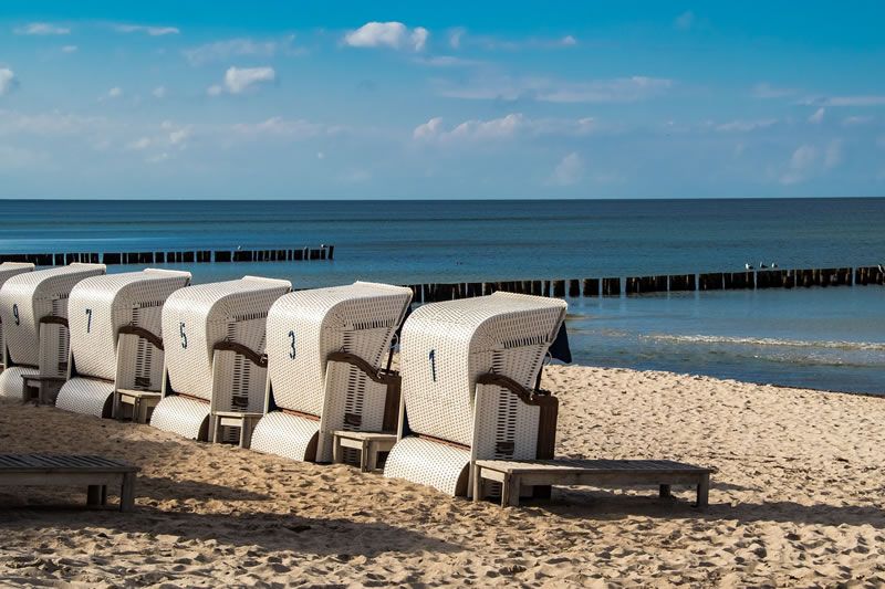 Reihe von weißen Strandkörben am Sandstrand mit Blick auf die ruhige See und einen blauen Himmel.