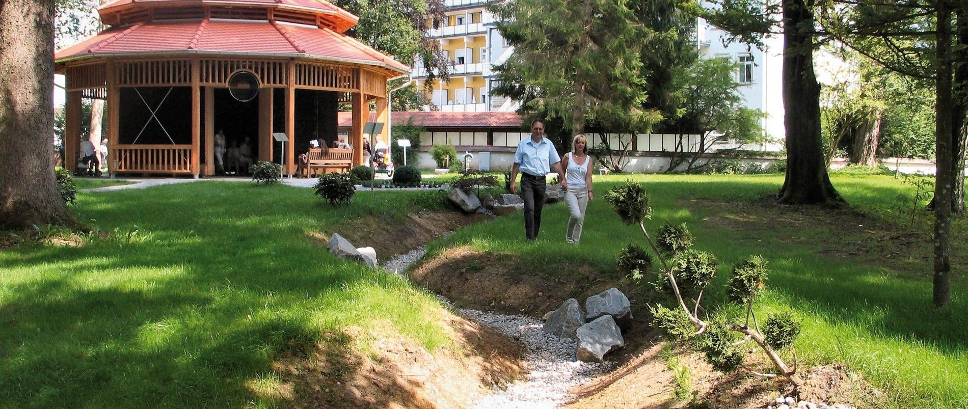 Ein Pavillon in einem Park mit zwei Menschen, die auf einem Weg spazieren gehen.
