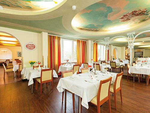 Elegantes Restaurant mit weiß gedeckten Tischen und kunstvoll bemalter Decke.