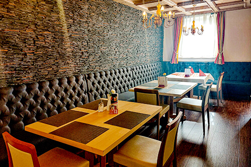 Gemütliches Restaurant mit Steinwand, gepolsterter Sitzbank, Holztischen und Kronleuchter.