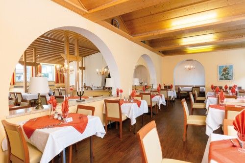 Elegantes Restaurant mit gedeckten Tischen, roten Servietten und Deckenleuchten, umgeben von gelben Wänden und Holzelementen.