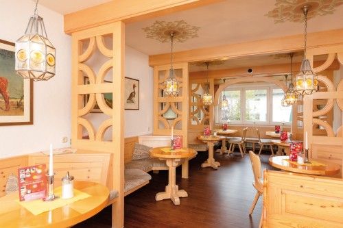 Gemütlicher Innenbereich eines Cafés mit Holztischen, Sitzbänken und dekorativen Leuchten.