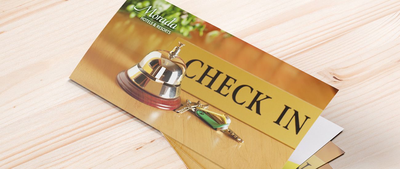 Einladendes Bild eines Empfangstresens mit einer Hotelglocke, einem 'Check In'-Schild und einem Schlüsselanhänger von Morada Hotels & Resorts.